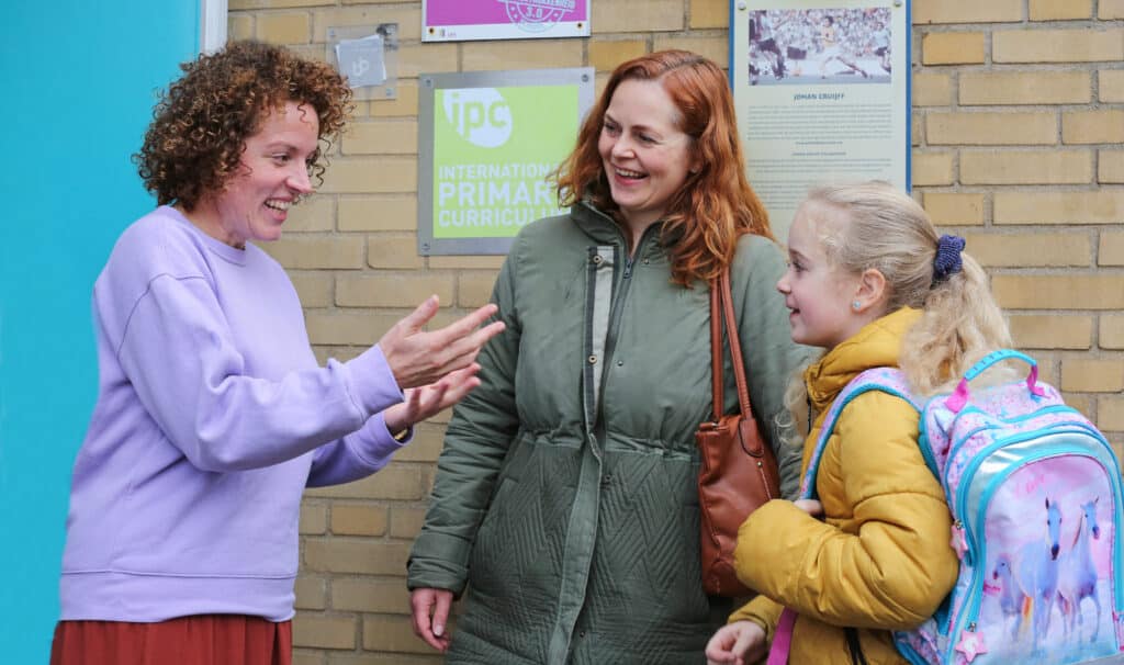 Communiceren met ouders, juf in gesprek met moeder en leerling bij schooldeur.